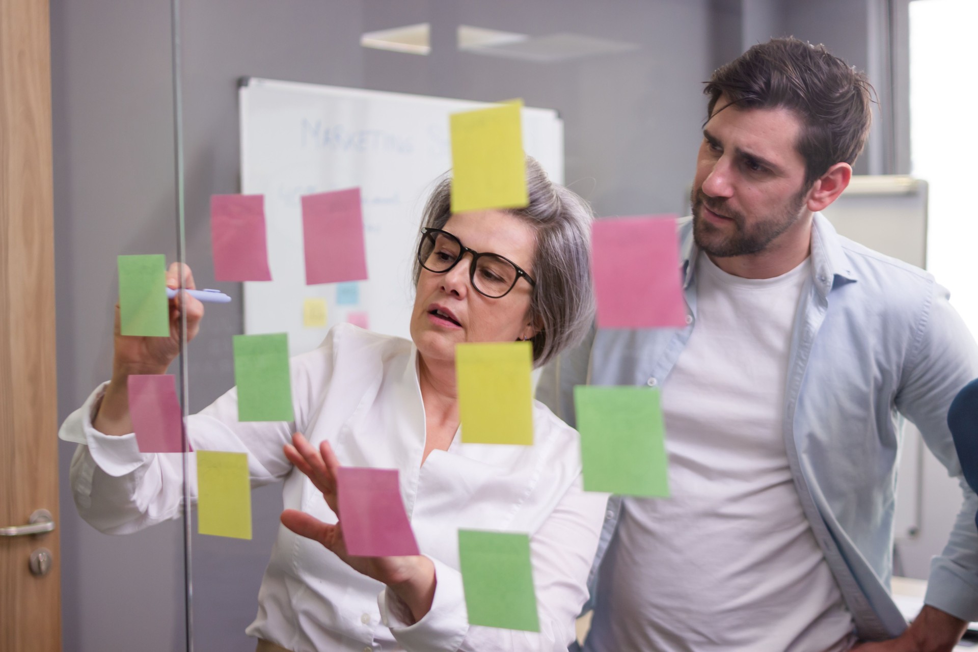Empresarios que planifican la estrategia utilizando notas adhesivas en la pared de vidrio en el espacio de coworking
